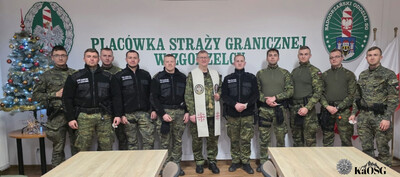 kapelan kaosg w sali odpraw stoi w szeregu z funkcjonariuszami kaosg na tle napisu placówka sg w zgorzelcu obok choinka, na ścianie logo sg i nadodrzańskiego osg