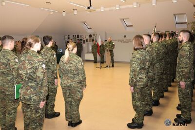 Ujęcie z boku sali podczas przemówienia komendanta. Funkcjonariusze stoją w równych szeregach, zachowując powagę uroczystości.