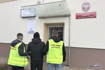 dwóch funkcjonariuszy w stroju cywilnym w kamizelkach odblaskowych z napisem straż graniczna polish border guard prowadzi do siedziby grupy zamiejscowej w oświęcimiu zatrzymanego obywatela turkmenistanu