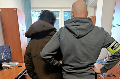 Funkcjonariusz ubrany po cywilnemu stoi z zatrzymanym obcokrajowcem w pomieszczeniu służbowym.