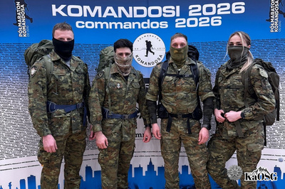 Czwórka reprezentantów Karpackiego Oddziału stoi w umundurowaniu polowym z zasłoniętymi twarzami na tle baneru bieg komandosa