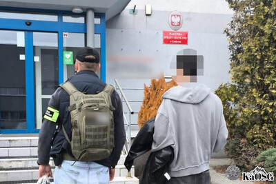 zatrzymany cudzoziemiec w szarej bluzie idzie do wejścia do placówki sg w krakowie w  asyście nieumundurowanego funkcjonariusza straży granicznej