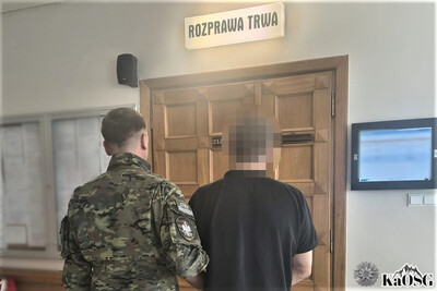 korytarz sądowy. przed wejściem na salę rozpraw w zakopiańskim sądzie stoi funkcjonariusz straży granicznej. obok niego zatrzymany obywatel ukrainy
