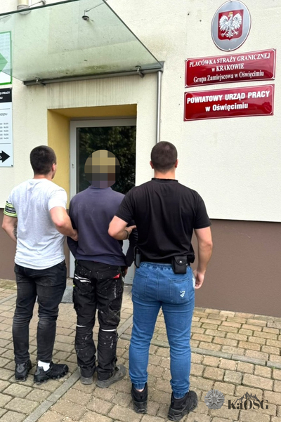 Na zdjęciu widać trzech mężczyzn. Stoją przed budynkiem gdzie prowadzą mężczyznę który stoi w środku.