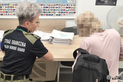 Dwie kobiety siedzą przy biurku tyłem. Kobieta po prawej stronie ubrana jest w mundur i daje kobiecie po prawej stronie do przeczytania dokument.