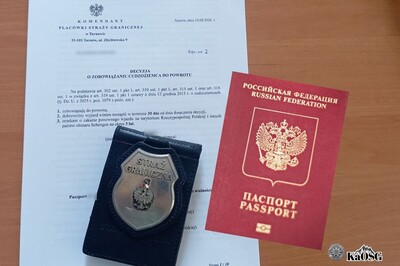 na biurku leży decyzja o zobowiązaniu do powrotu, odznaka funkcjonariusza straży granicznej oraz okładka paszportu federacji rosyjskiej